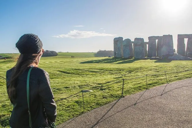 A visitor in a warm jacket looking at Stonehenge from the path